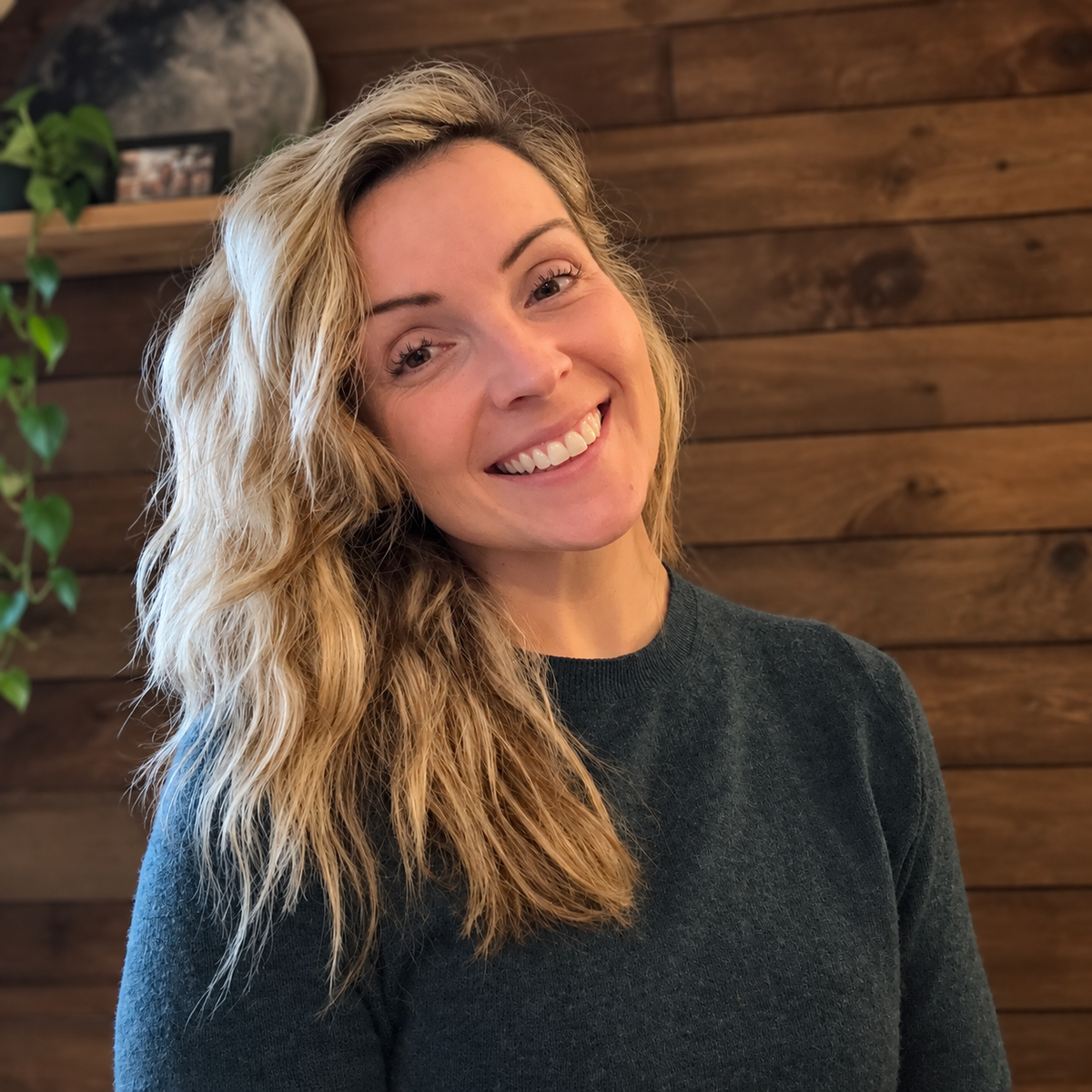 Femme souriante aux cheveux blonds devant un mur en bois