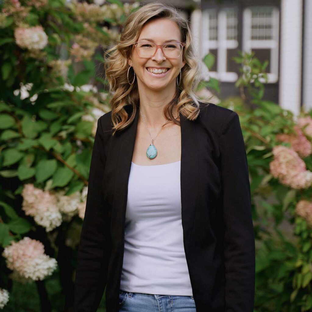 Femme souriante en tenue décontractée parmi des fleurs.
